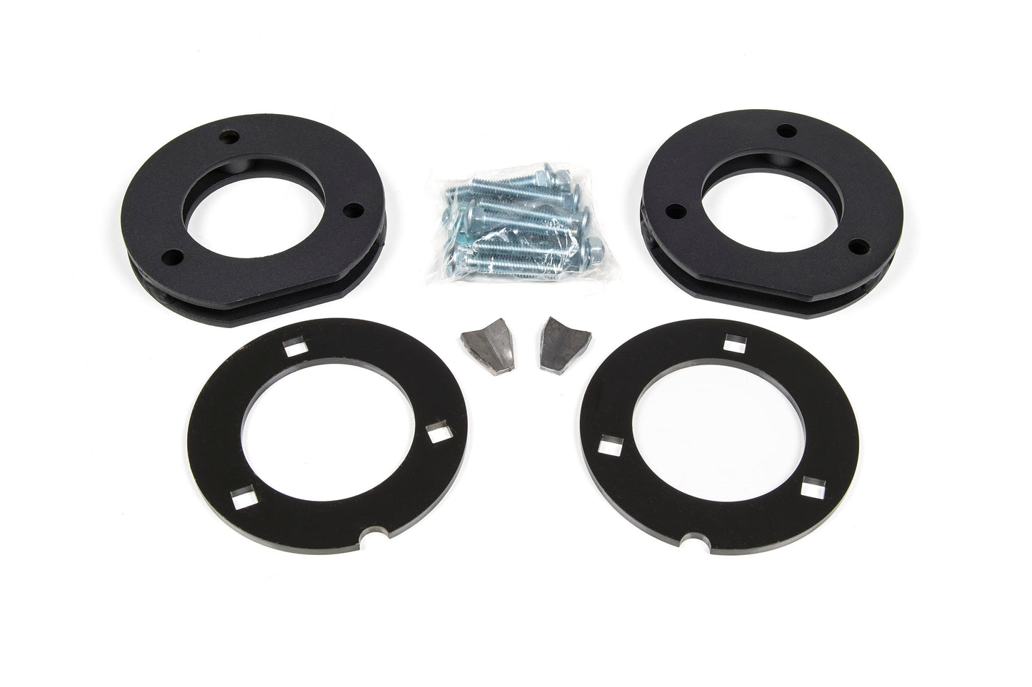 A set of black circular metal plates from the BDS 2 Inch Leveling Kit for the 2014-2018 Chevy Silverado or GMC Sierra 1500 are arranged in pairs on a white background. A plastic bag containing screws and bolts is placed in the center, with two small metal pieces situated below.