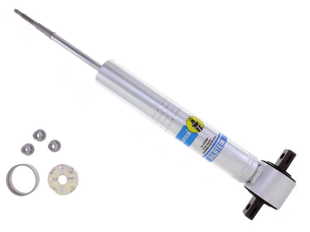 A Bilstein Shocks B8 5100 Series 07-18 GM 1500 Front Shock Absorber, along with its accompanying hardware (nuts, a washer, and a mounting plate), is displayed on a white background. The monotube shock absorber features a silver body with the Bilstein logo and branding, and it is Ride Height Adjustable for enhanced performance.